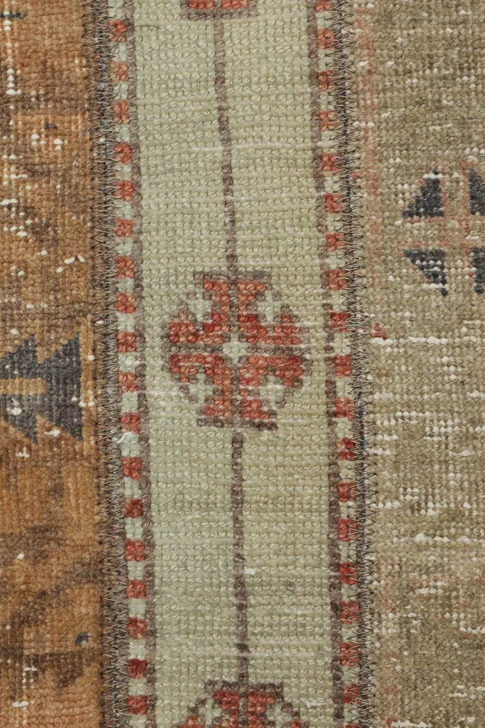 Macro detail of a rust and green geometric motif within the rug's stripe