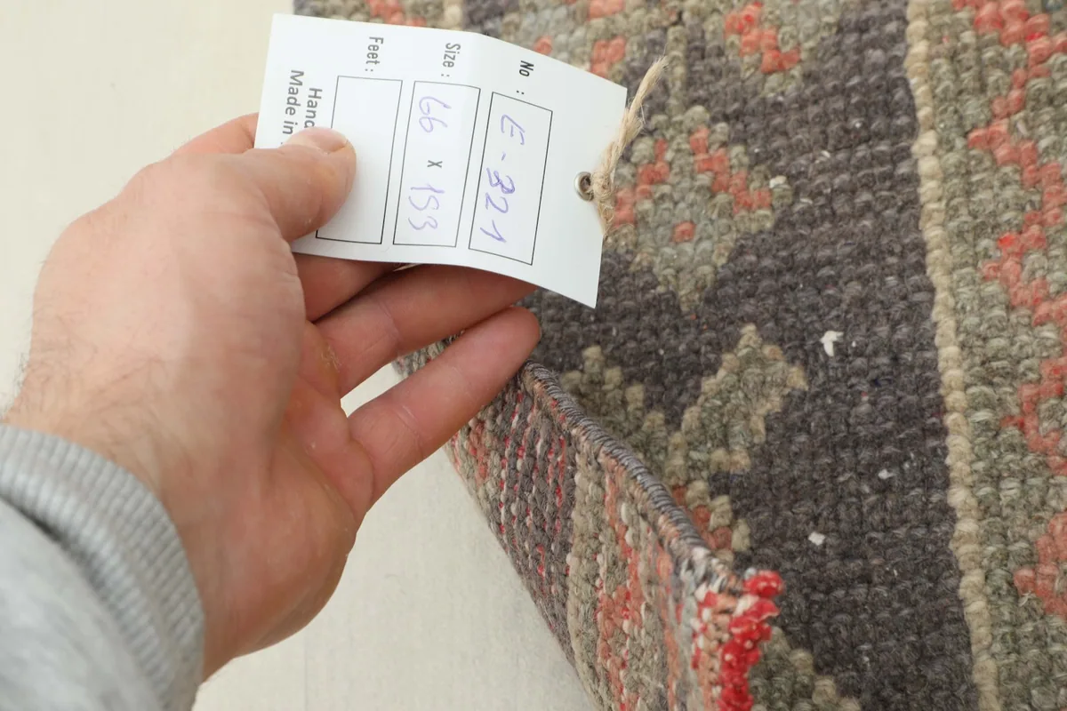 A hand holding a tag with the rug's dimensions (66 x 153 cm) and identifying number.