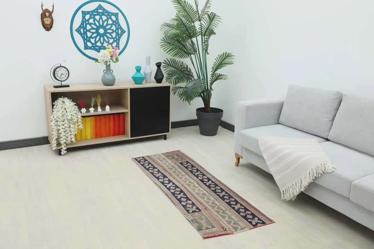 Vintage runner rug in a hallway setting, showing its length and colors next to a sofa and cabinet