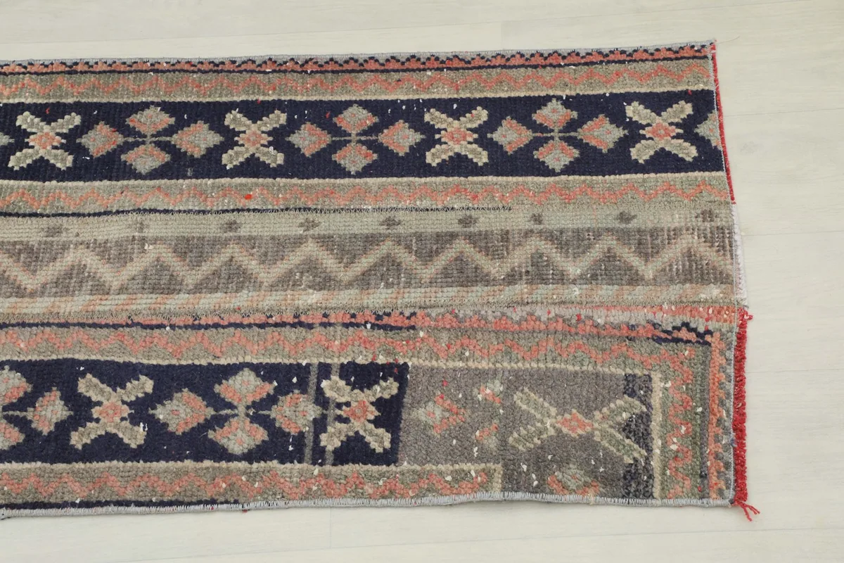 Close-up detail of one end of the rug, showing navy and rust geometric motifs and a gray striped section
