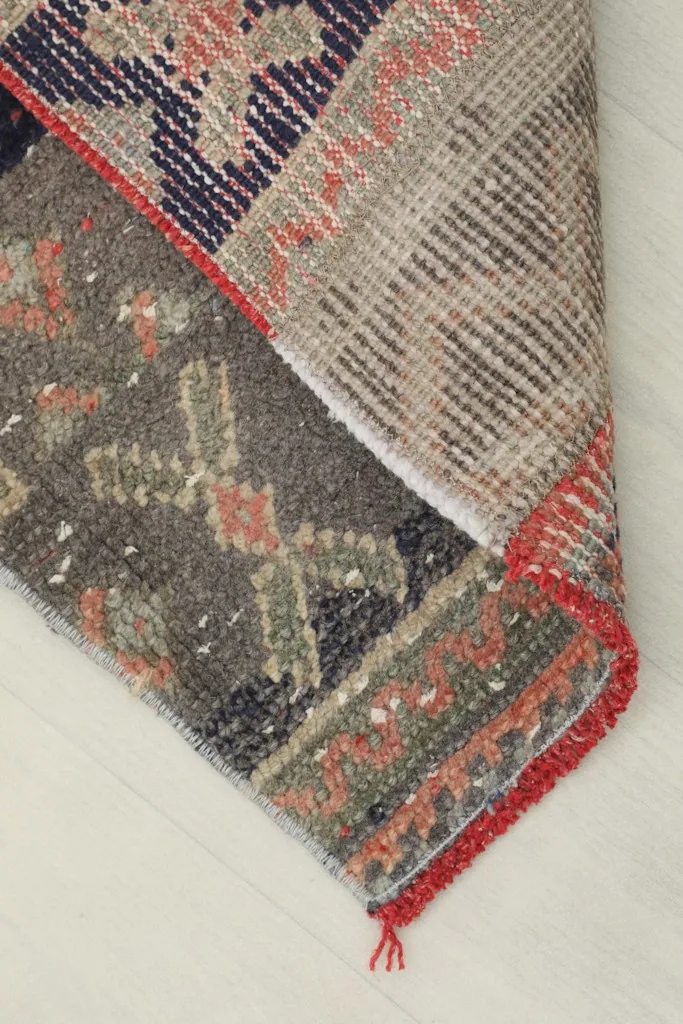View of the back of the rug, showing the cotton foundation and hand-knotted construction, with a folded corner
