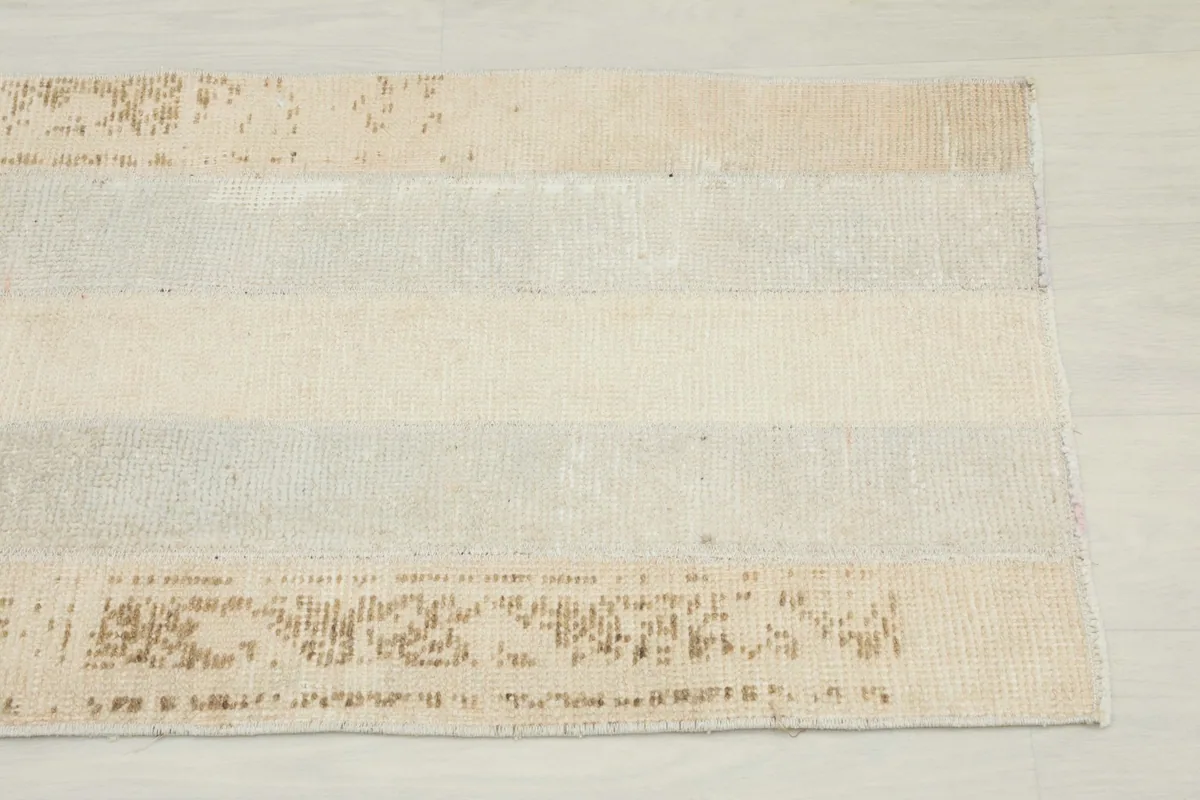 Close-up view of the rug's patchwork design with beige, gray, and faded rust patterns
