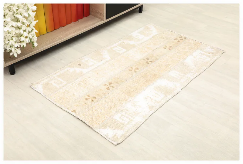 Full overhead view of the beige and tan vintage Anatolian rug on a white floor next to a bookshelf