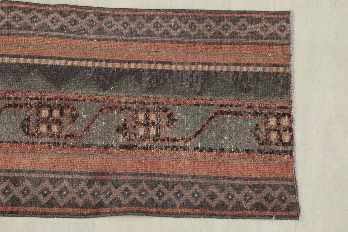 One end of the rug, highlighting the rust and brown striped border with small geometric patterns