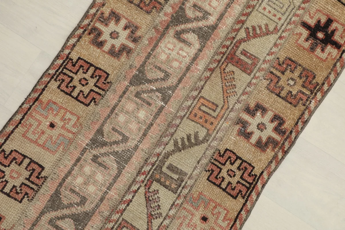 Close-up detail of the rug's surface, highlighting the tan, rose, and brown geometric motifs and texture.