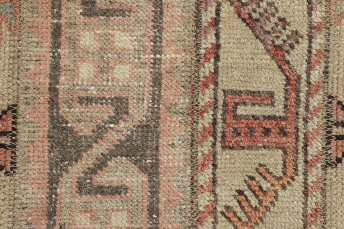 Very close detail shot of the hand-knotted wool pile and specific geometric elements in rose and brown.