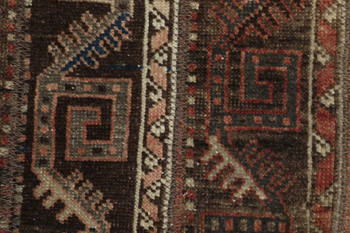Close-up detail of the hand-knotted wool pile, showing individual geometric motifs in brown, rust, and pink.