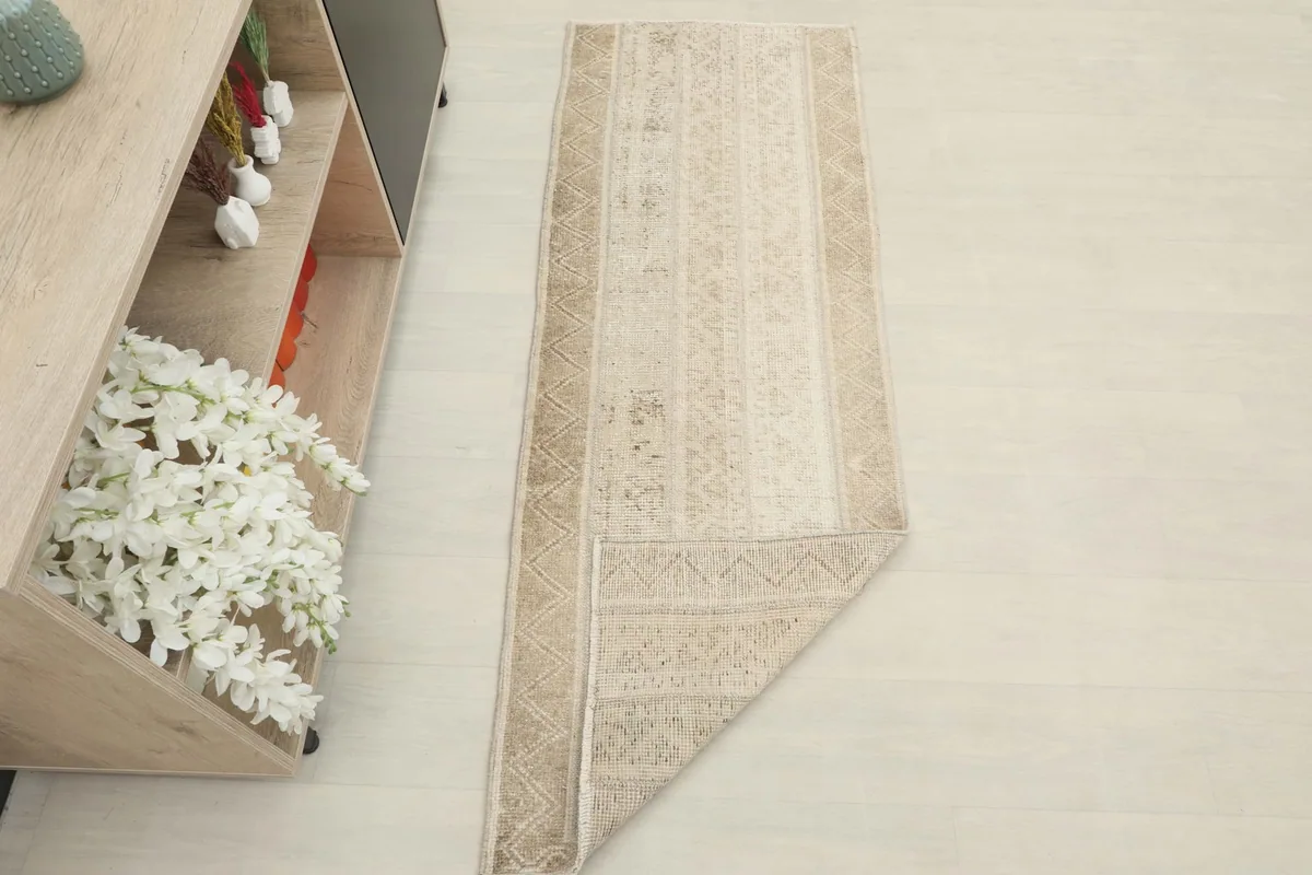 The runner rug partially folded in a room setting, next to a cabinet with decor.