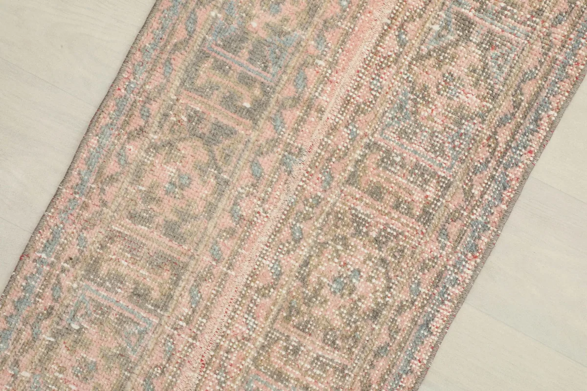 Close-up of the runner's surface, highlighting the geometric motifs and faded rose and gray colors.