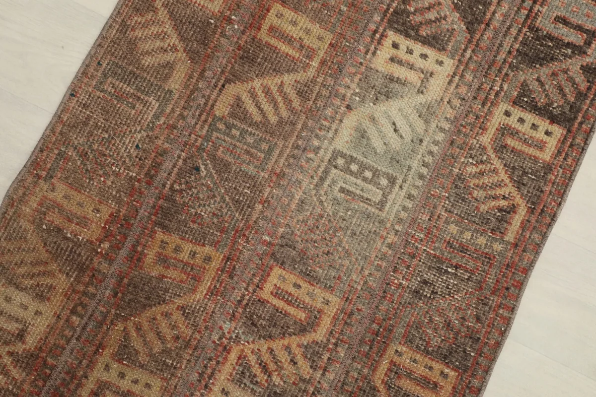 Close-up detail of the rug's surface, showing brown, rust, and tan geometric motifs and wool pile