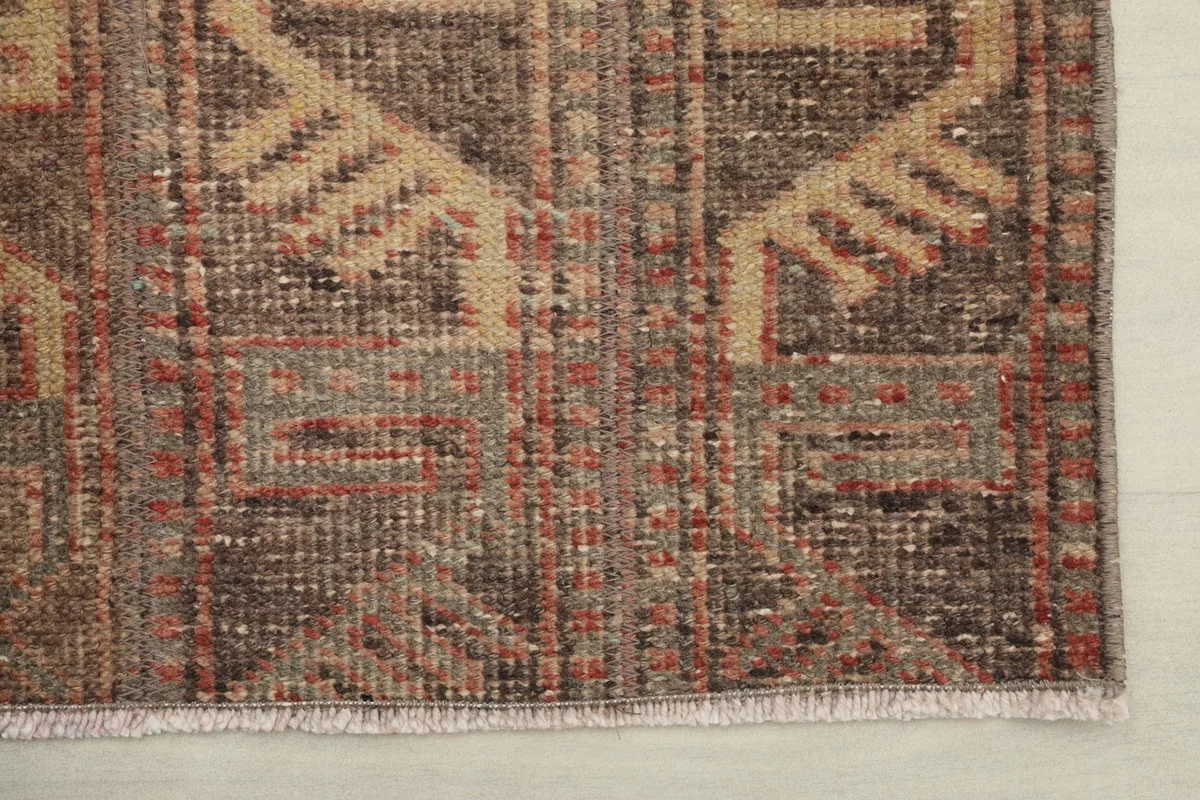 Detail of the rug's edge and fringe, showing the hand-knotted construction and worn finish