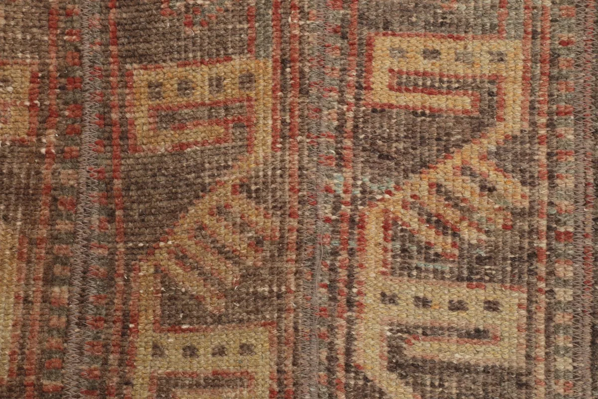 Extreme close-up of the low wool pile, revealing individual knots and color variations in brown and rust