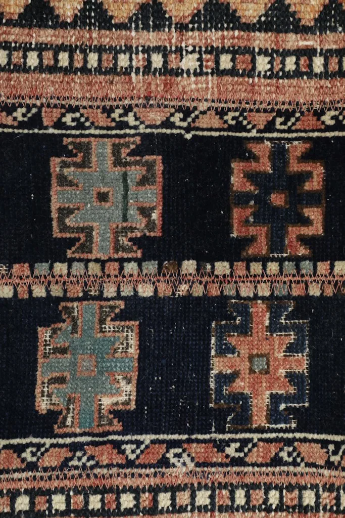 Tight detail of the hand-knotted wool pile and individual geometric motifs in navy, rust, and gray.
