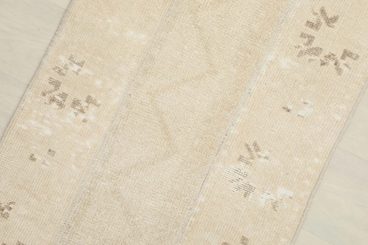 Close-up of the beige rug's surface, showing the low pile and faded tan geometric motifs.