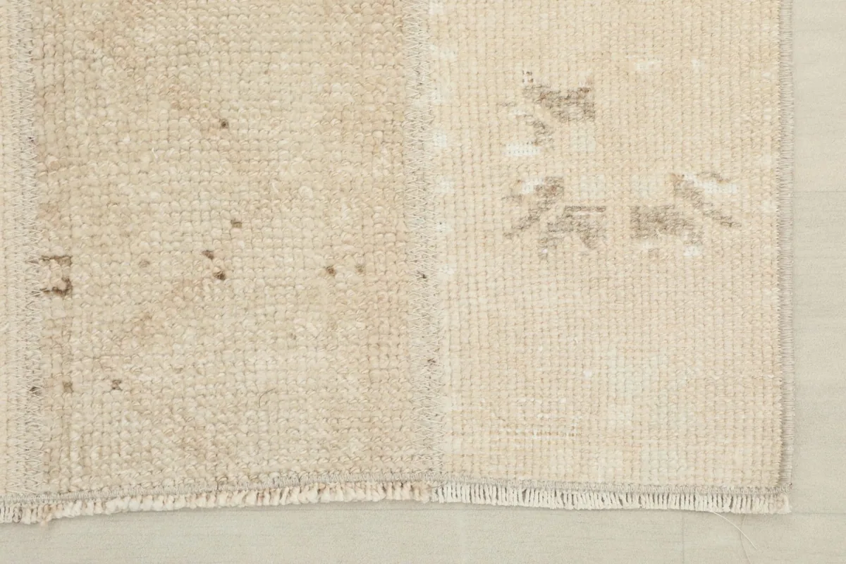Detail of the rug's end, highlighting the fringed edge and variations in the beige and tan colors.