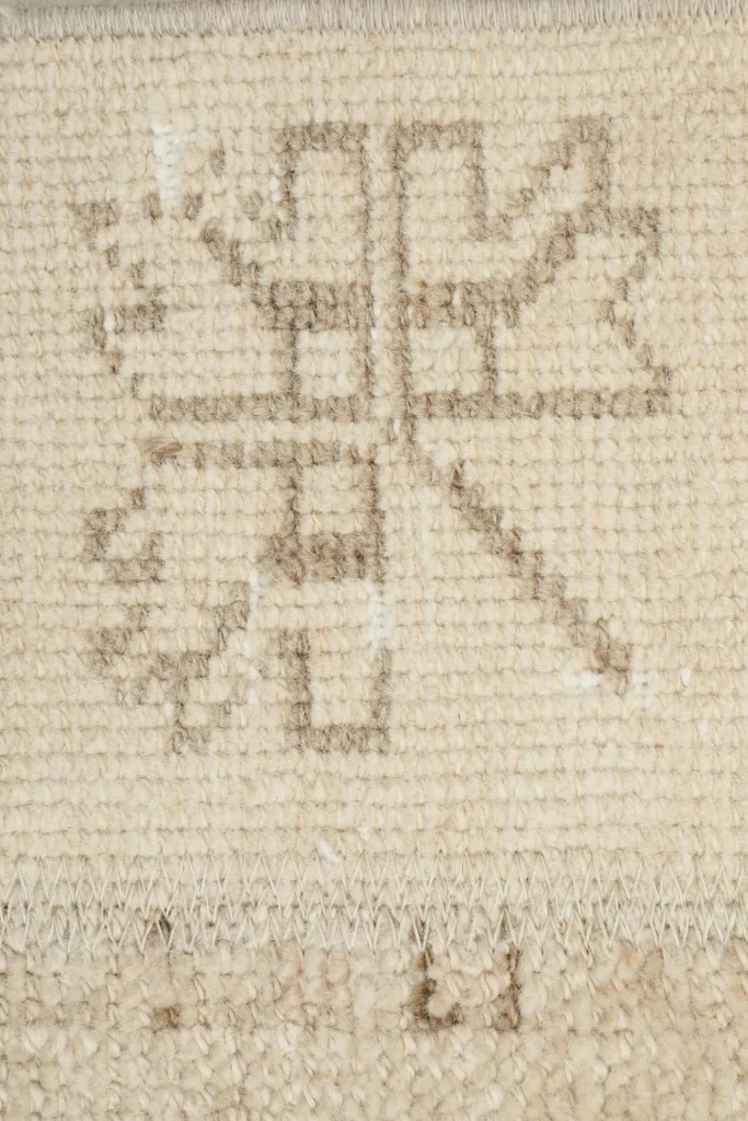 Macro detail of a distinct tribal geometric motif in tan and gray on the beige field.