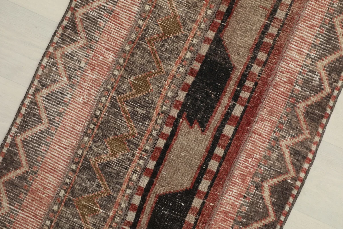 Close-up detail of the rug's surface, showing various geometric motifs in rose, brown, and black tones.