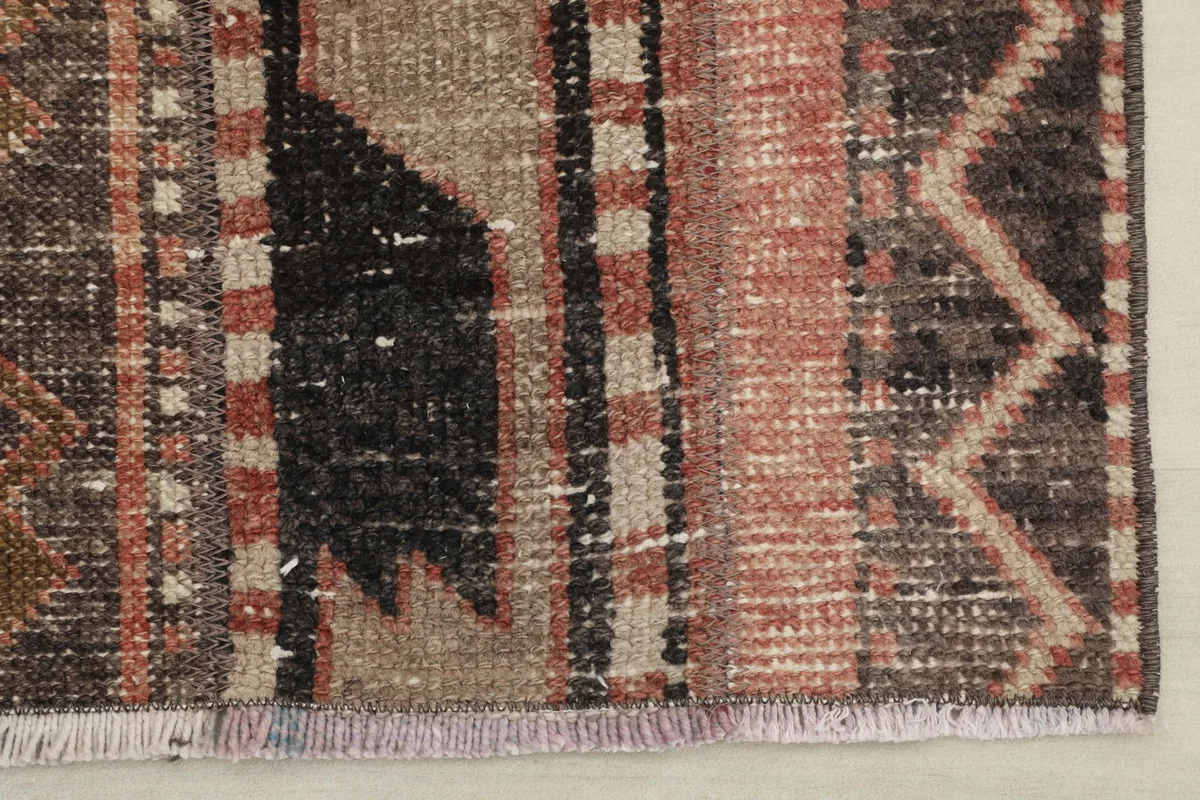 Close-up of one end of the rug, showing the short fringe and the worn texture of the pile.