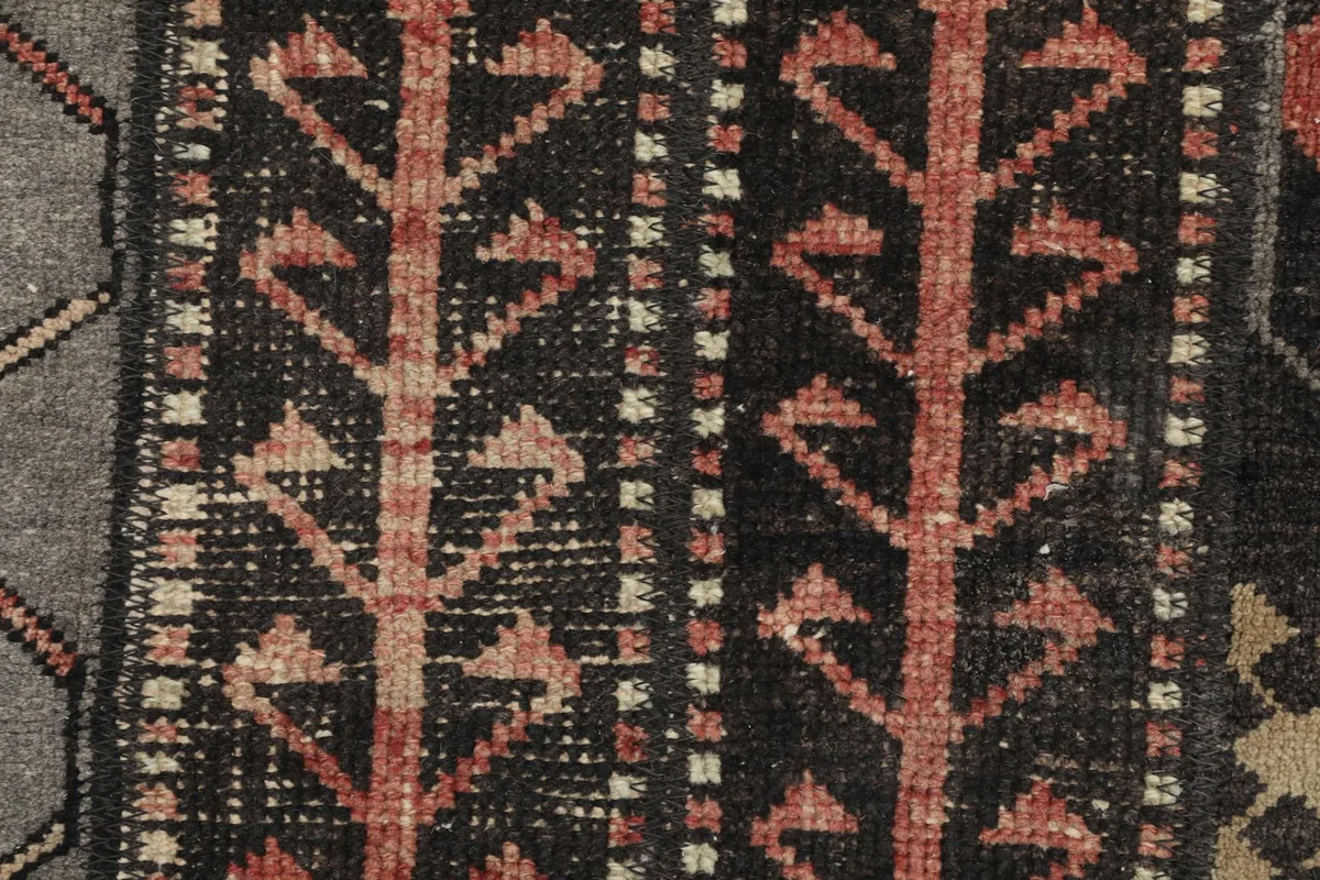 Detailed view of the hand-knotted wool pile and tree-like tribal motifs in rust and black