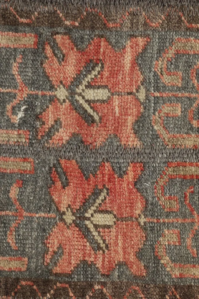 Detailed view of the rose and tan geometric patterns on the rug's charcoal field