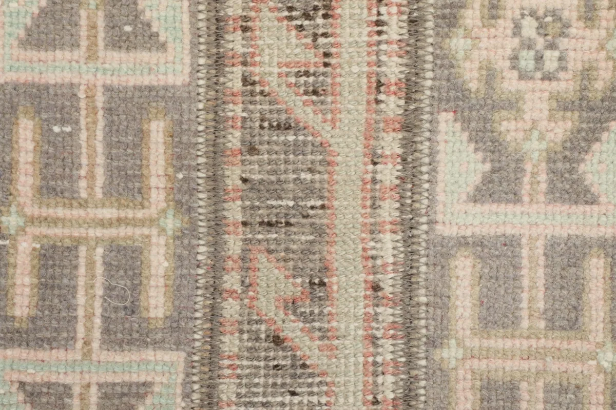 Detailed view of the hand-knotted wool pile showing gray, rose, and olive motifs