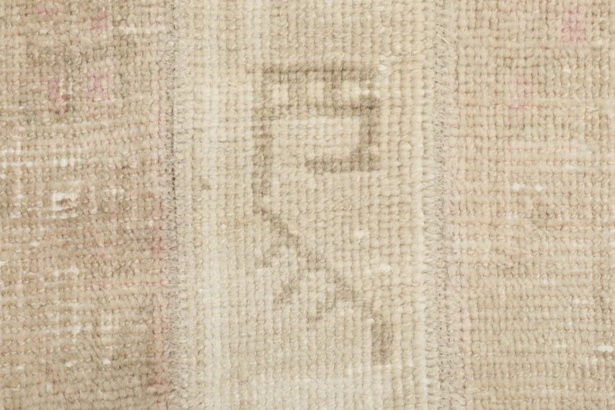 Detailed close-up of a tribal geometric motif within a beige patch of the hand-knotted rug