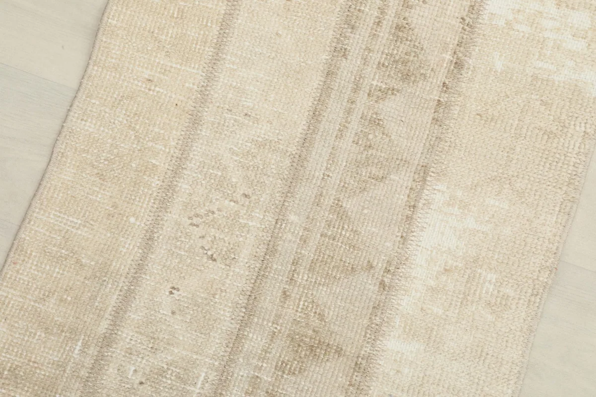 Close-up detail of the rug's surface, highlighting the faded beige colors and low pile