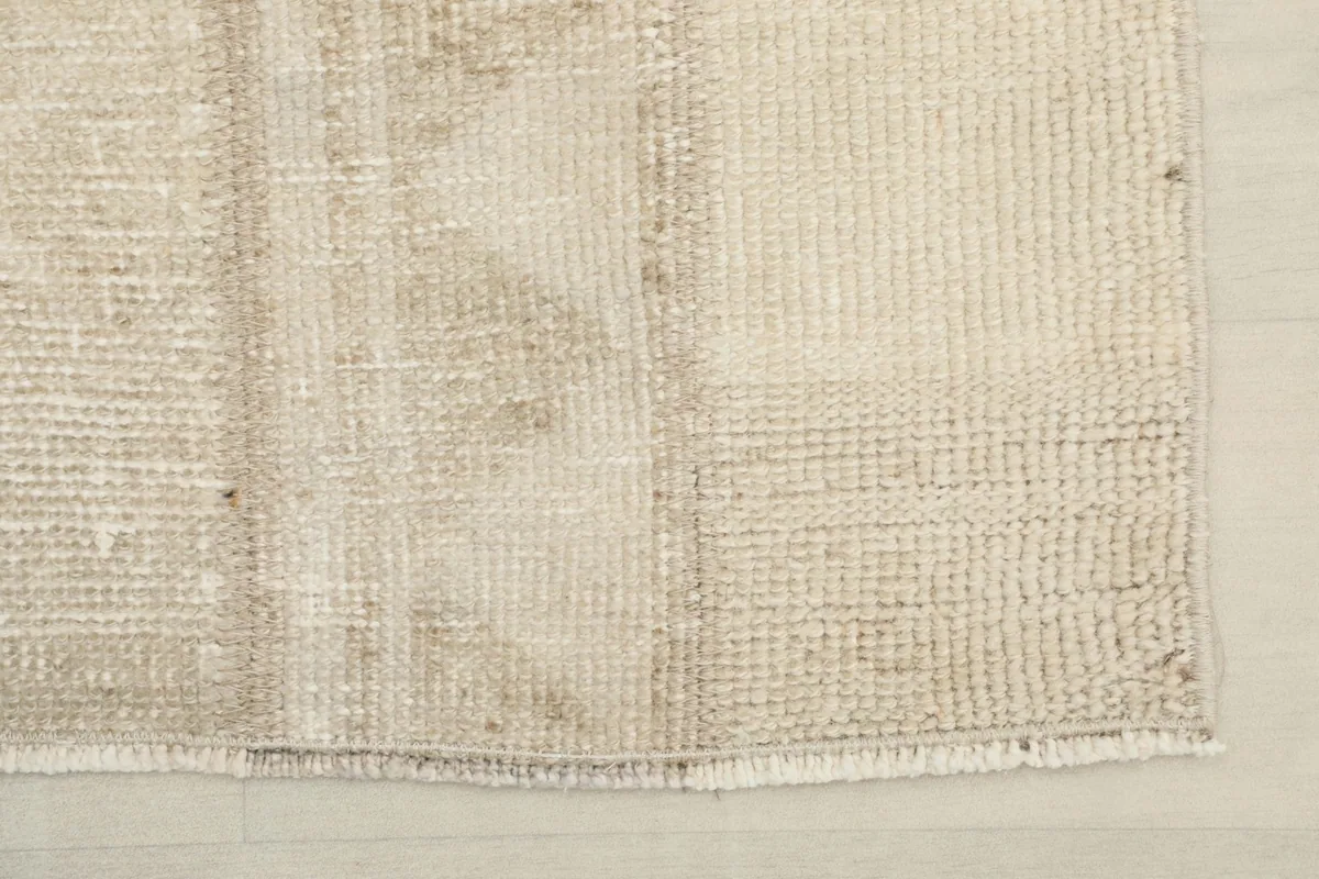View of the short, natural fringe and one corner of the distressed beige vintage rug
