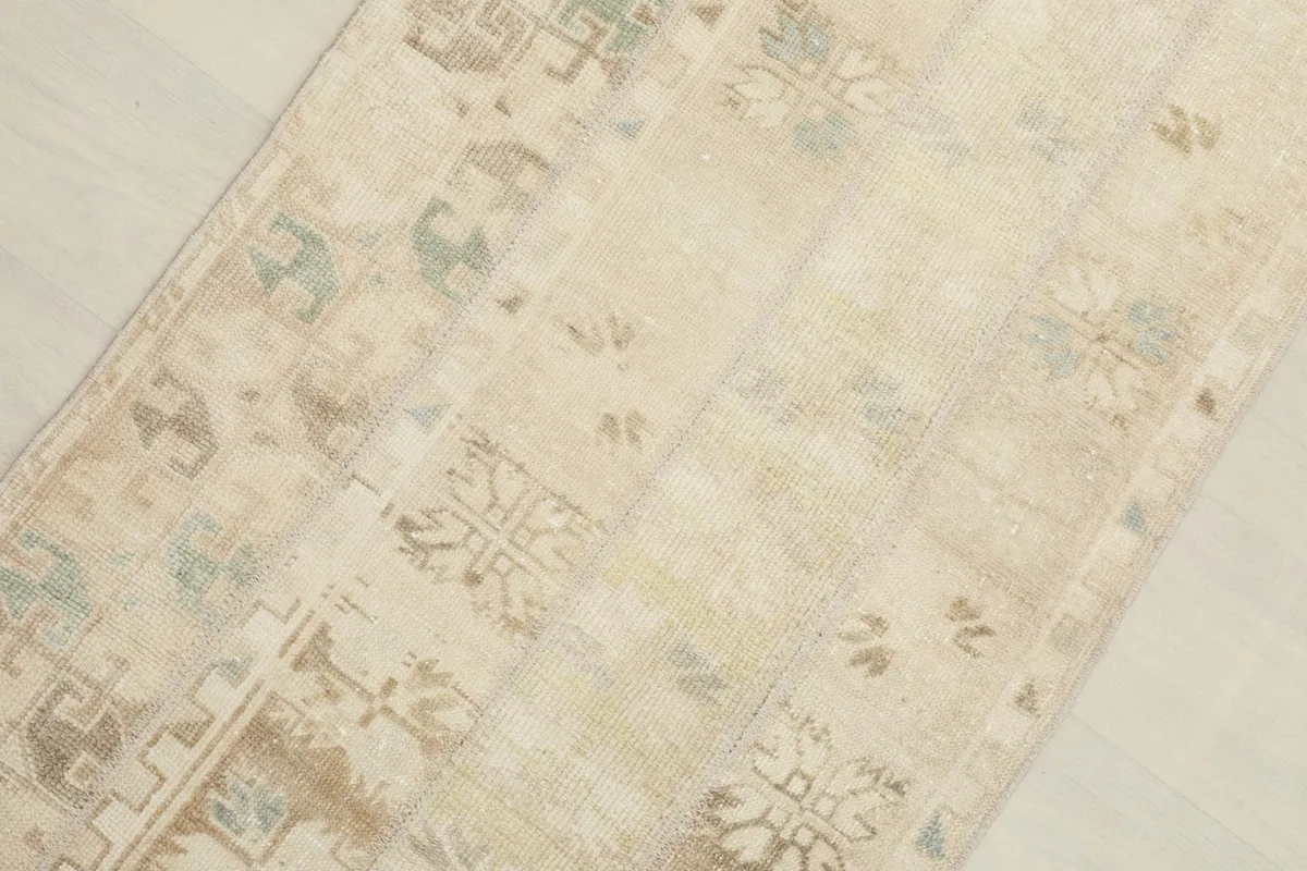 Close-up of the rug's surface, highlighting the beige, brown, blue, and green geometric motifs