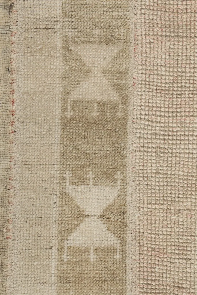 Detailed view of the hand-knotted wool pile, showing texture and subtle variations in the beige and gray tones.