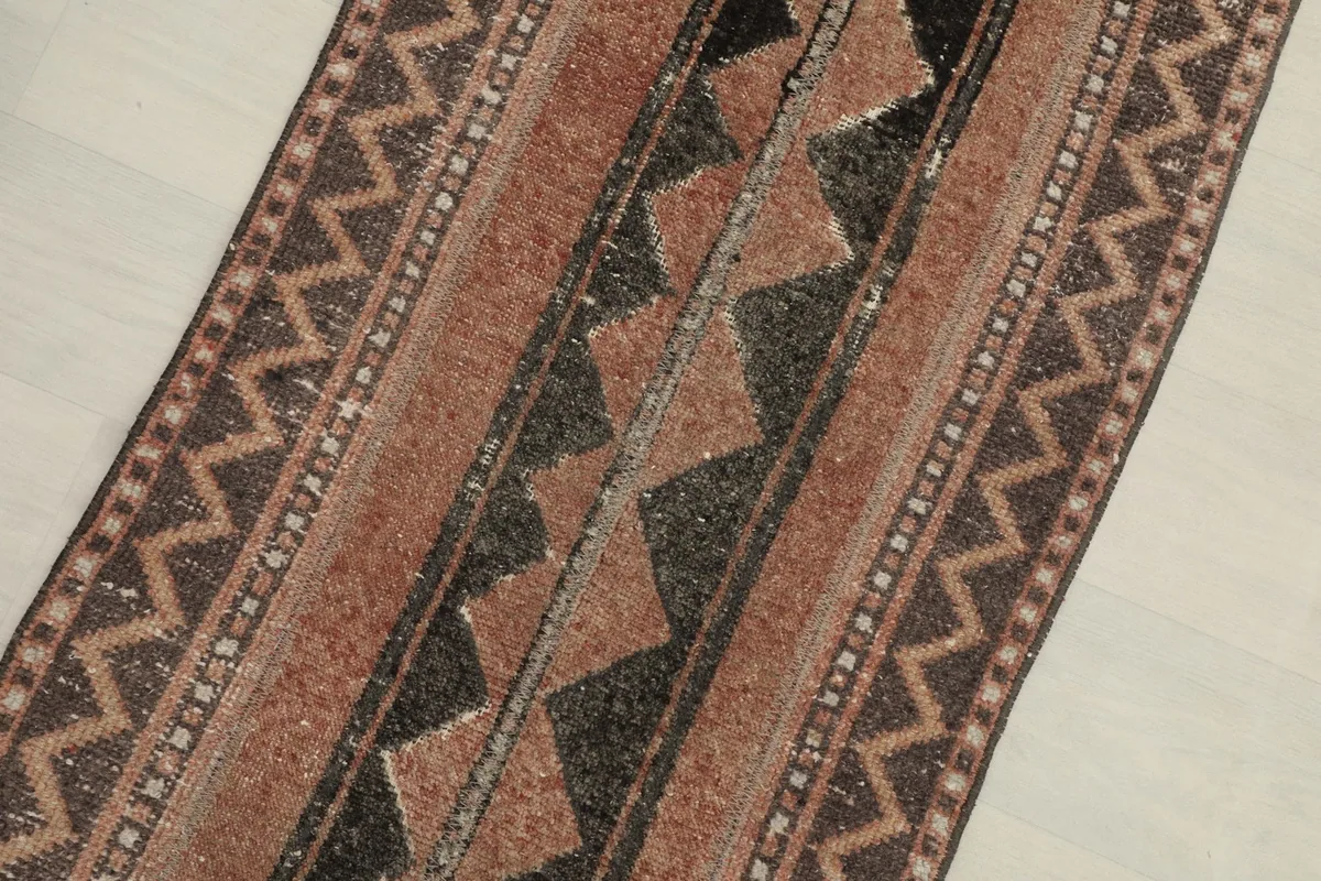 Close-up angled view highlighting the rust and black colors and geometric motifs of the rug.