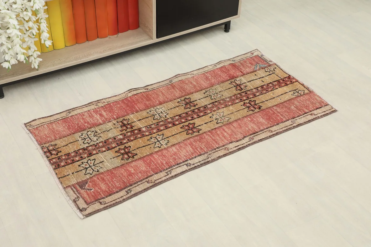 Angled view of the red and tan rug placed on a white floor next to a bookshelf