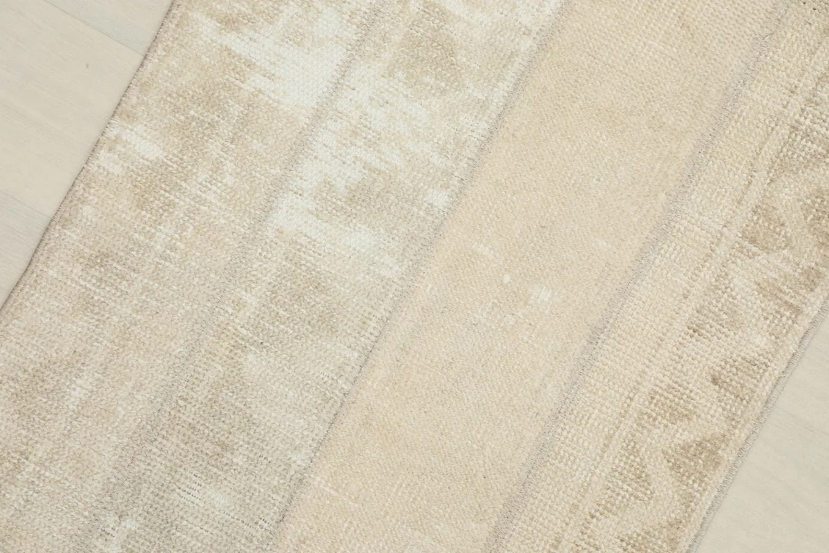 Close-up detail of the rug's surface, highlighting the subtle cream and beige tones and distressed areas.