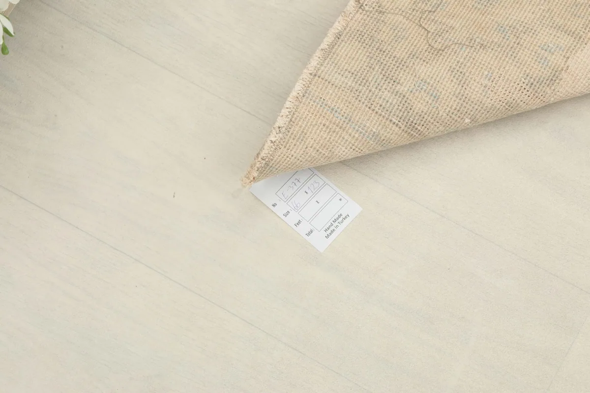 Corner of the rug lifted to show the product tag and the clean, light floor beneath.