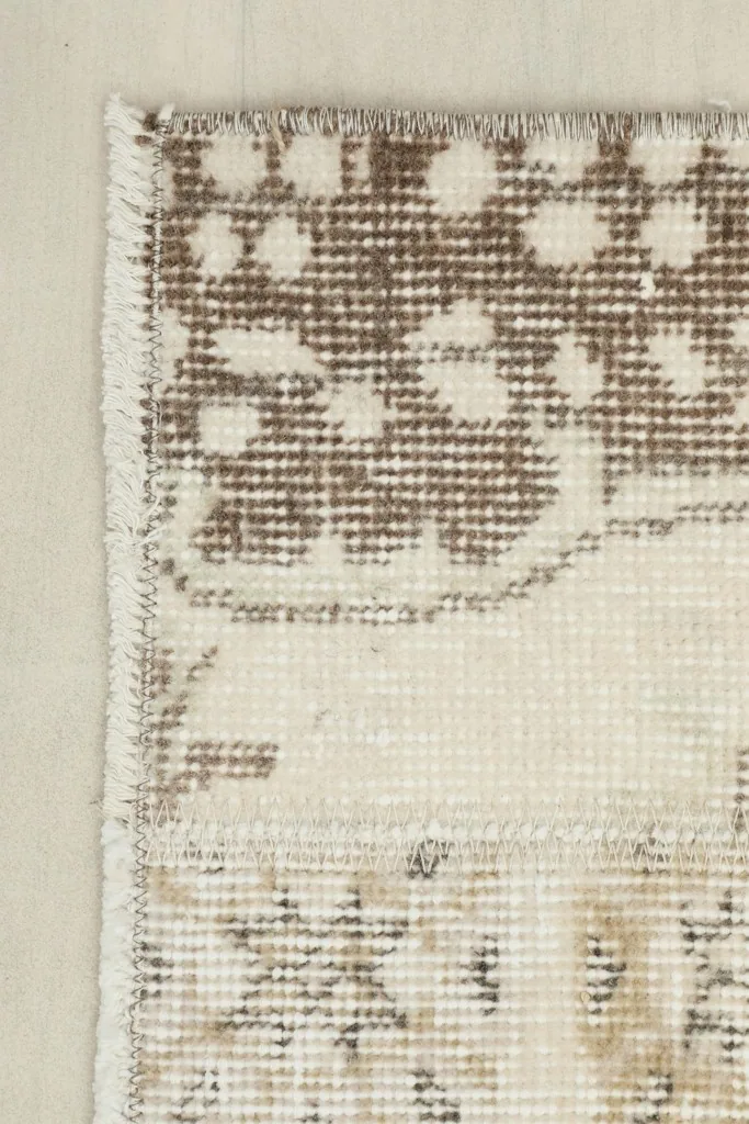 Corner detail of the rug, showing the brown border with small floral patterns and the subtle wear on the edge.