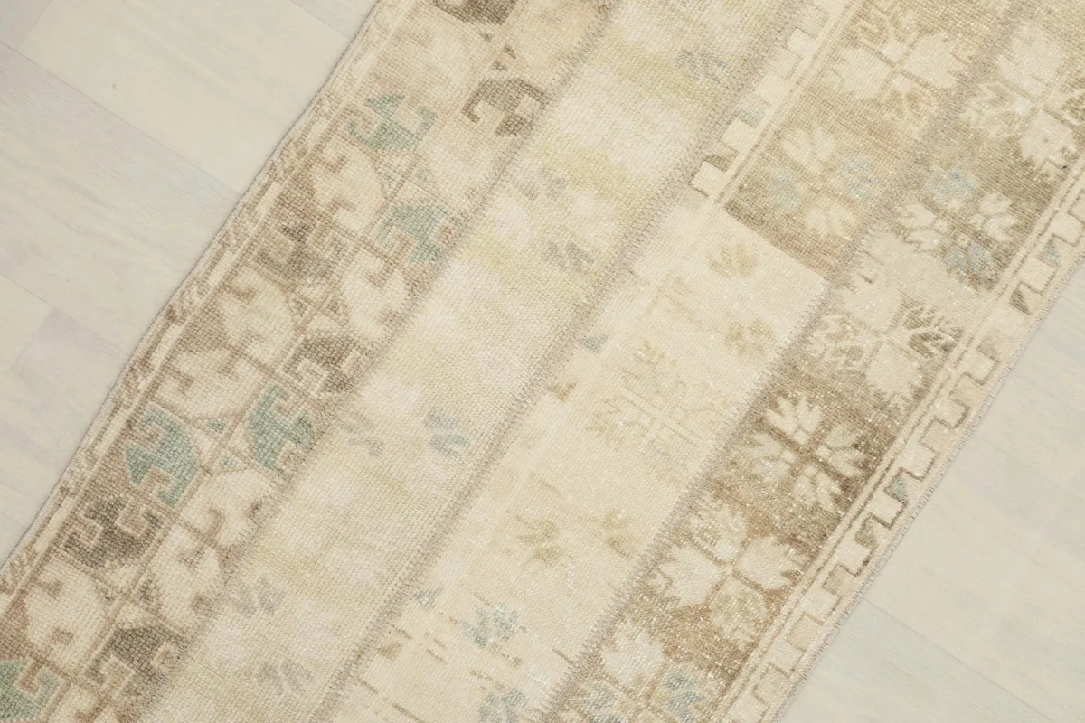 Close-up detail of the rug's patchwork sections, showing ivory, tan, and olive geometric patterns