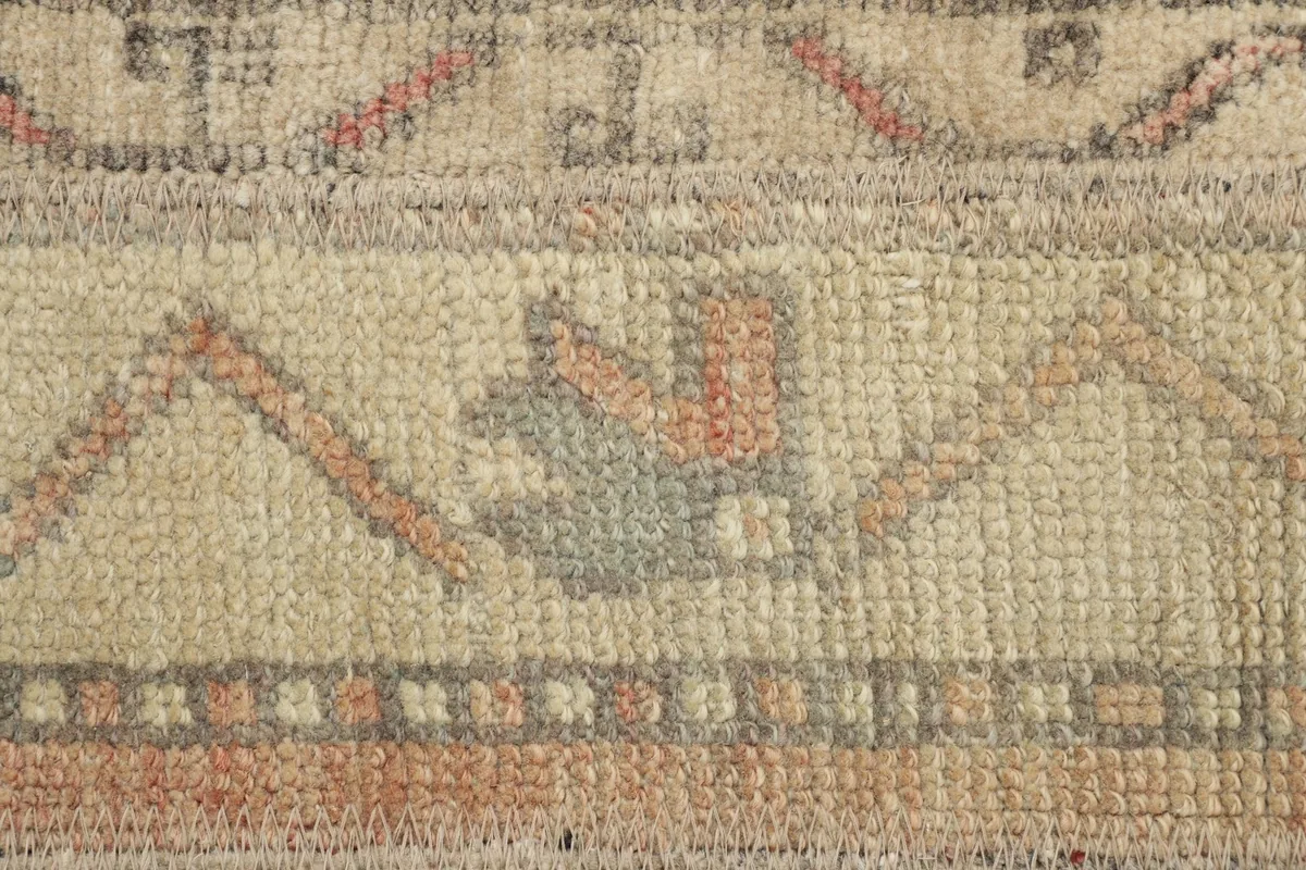 Detailed view of the rug's wool pile, highlighting rust, rose, and olive geometric patterns.