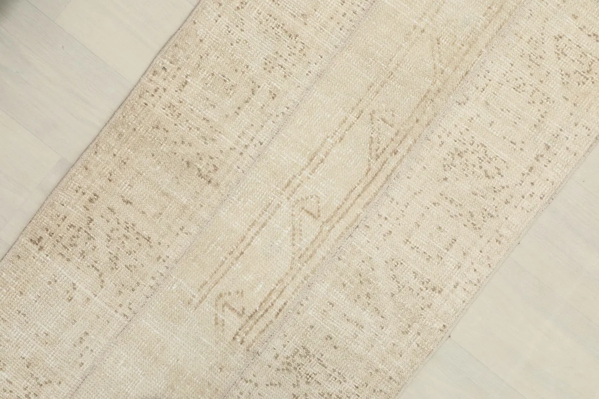Close-up detail of the rug's surface, highlighting the subtle tan geometric motifs on a cream field