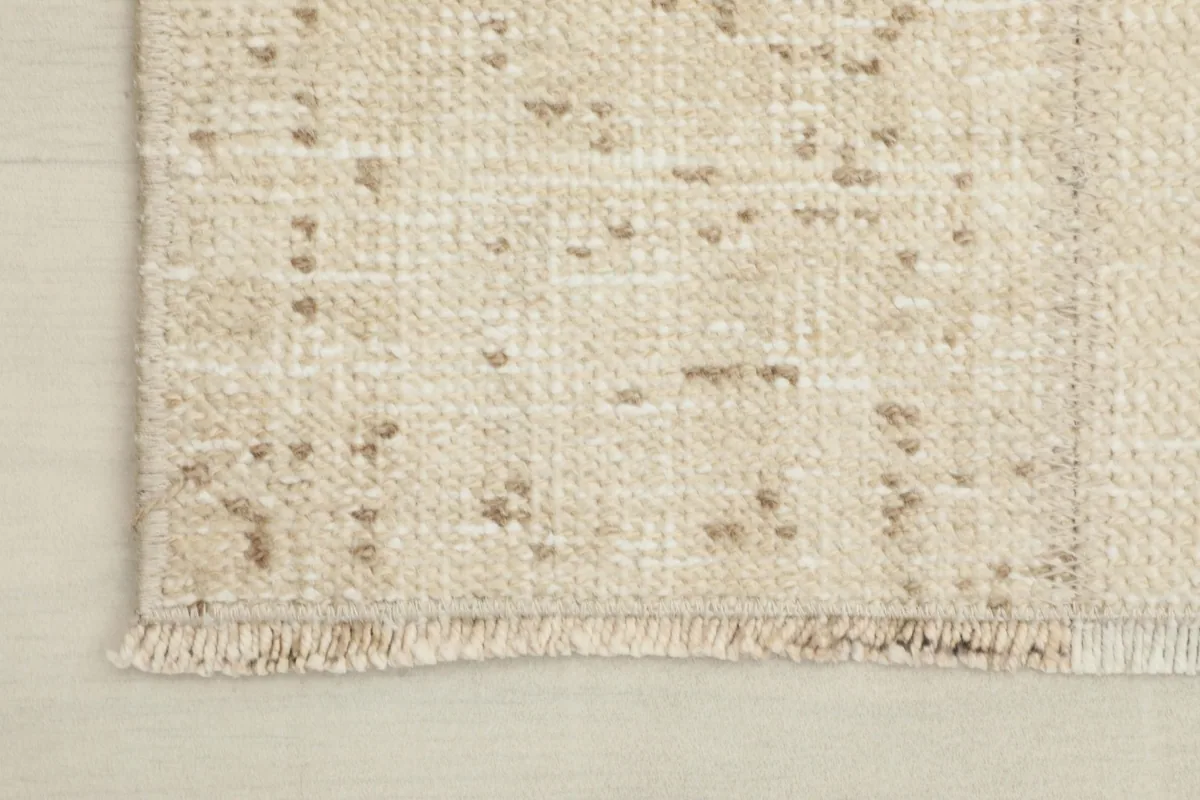 Close-up of the short, rustic fringe and edge of the cream and tan hand-knotted rug