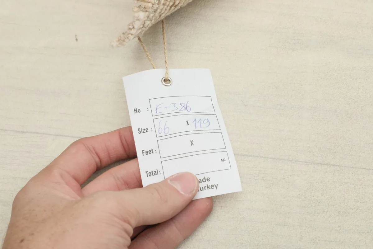 Hand holding a tag showing the rug's dimensions in centimeters and indicating its origin from Turkey