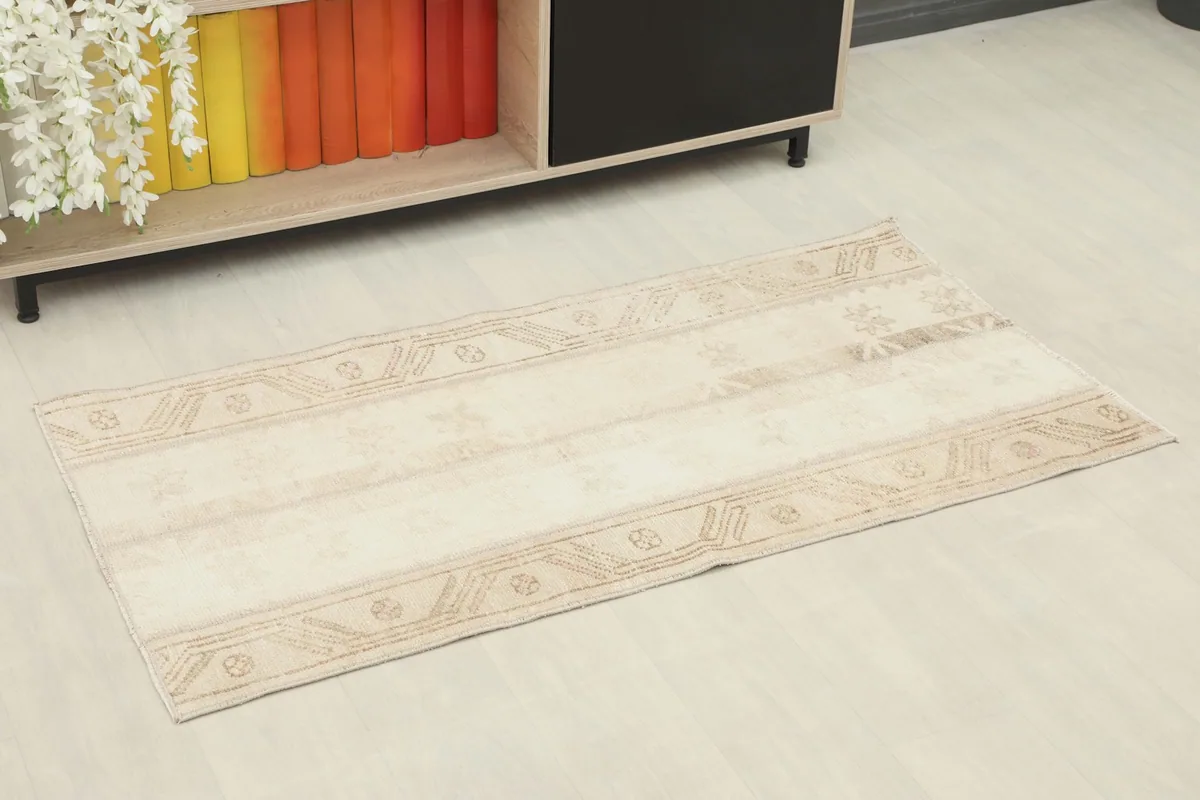 Angled view of the beige and tan vintage rug placed in a room setting next to a bookshelf