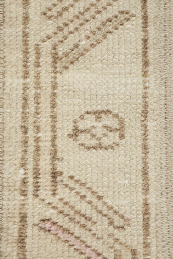 Detailed view of the hand-knotted wool pile and tan geometric motifs on the beige field