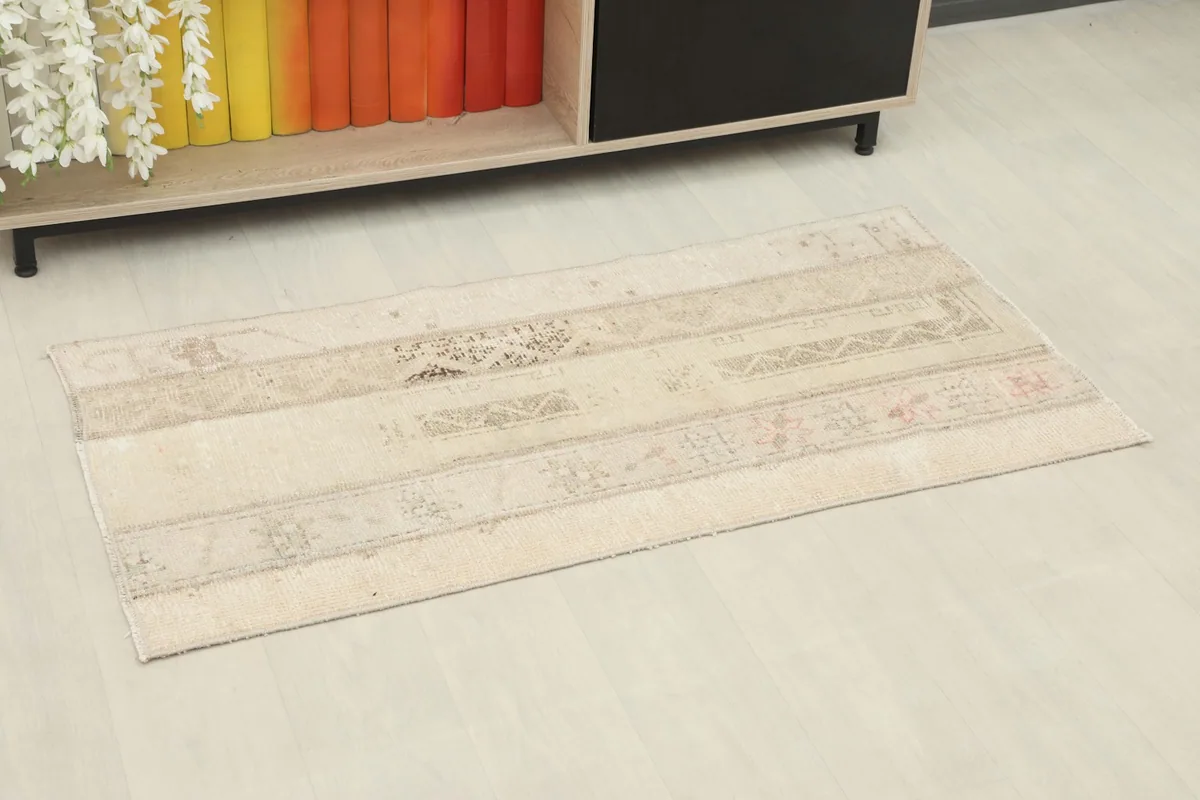 Beige patchwork area rug styled in a room setting with a wooden shelf and white floor.