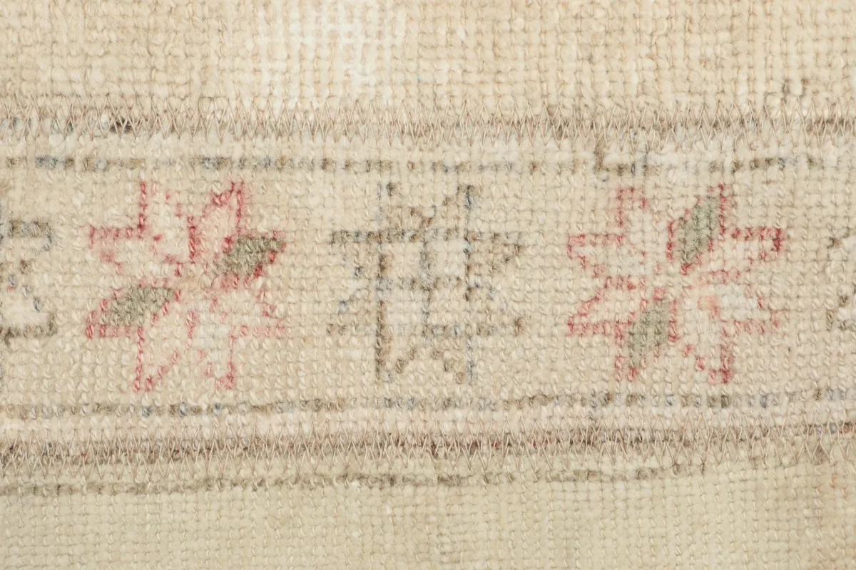 Close-up detail of faded rose and green geometric motifs within a beige patch of the rug.