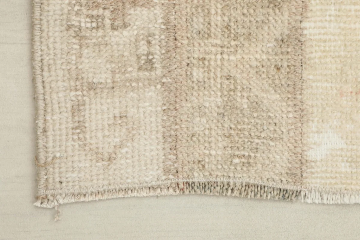 Close-up of a rug corner, showing the wool pile texture and a section of beige and brown patterns.