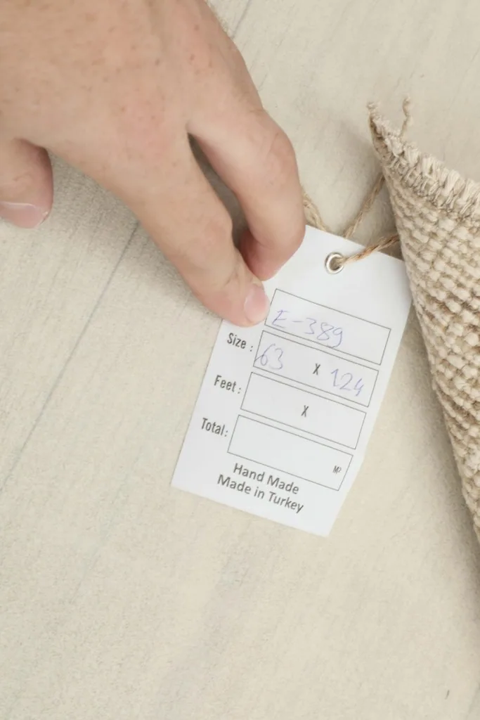 Hand holding a tag showing the rug's dimensions in centimeters, confirming its handmade origin from Turkey.