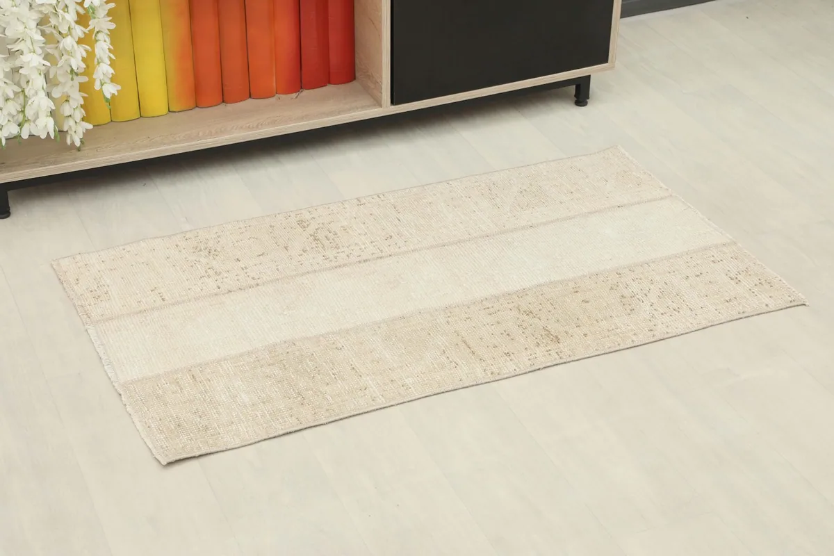 Beige patchwork vintage rug displayed on a light floor next to a low cabinet with books