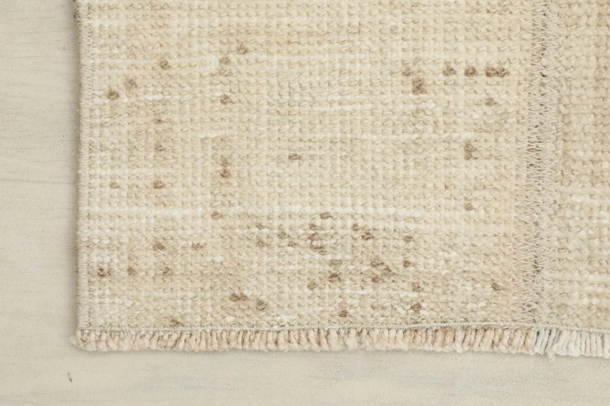 Corner of the rug showing the short fringes and the subtle variations in beige tones