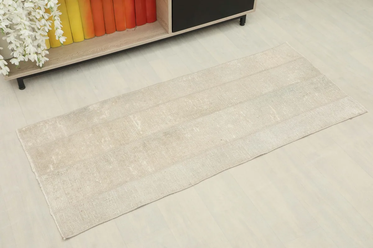 Angled view of the beige and cream vintage wool rug showing its distressed surface and subtle tonal variations.