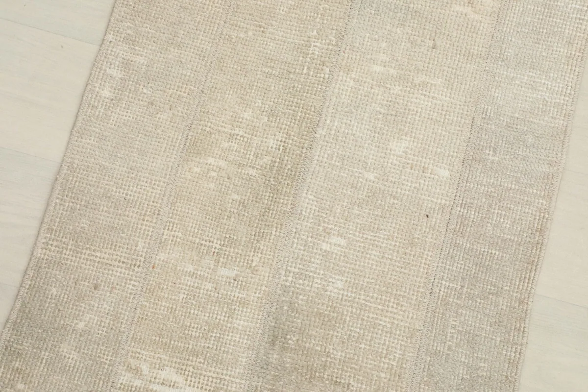 Close-up detail of the hand-knotted wool pile, highlighting the muted beige and gray distressed texture.